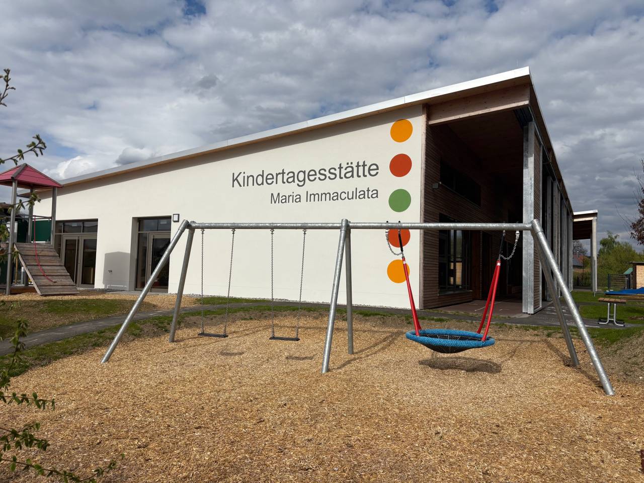Außenansicht des Kindergartens mit Schaukel und Spielplatz.