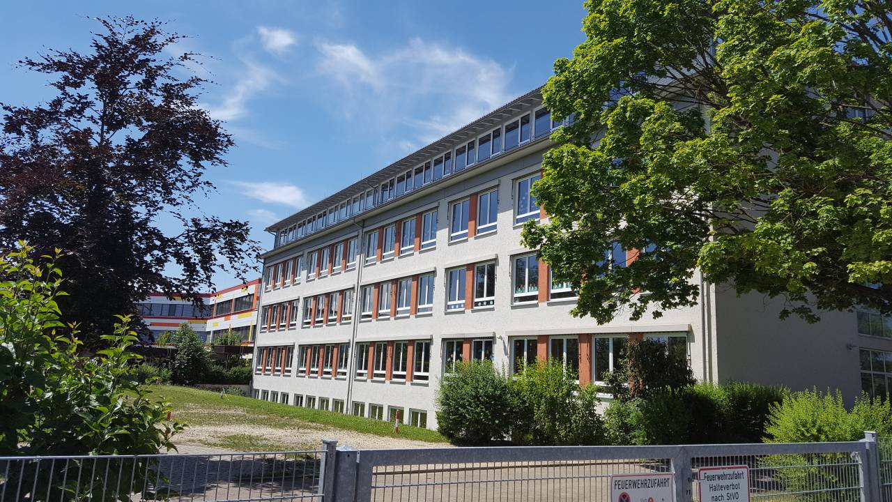 Schulgebäude mit Bäumen im Pausenhof.